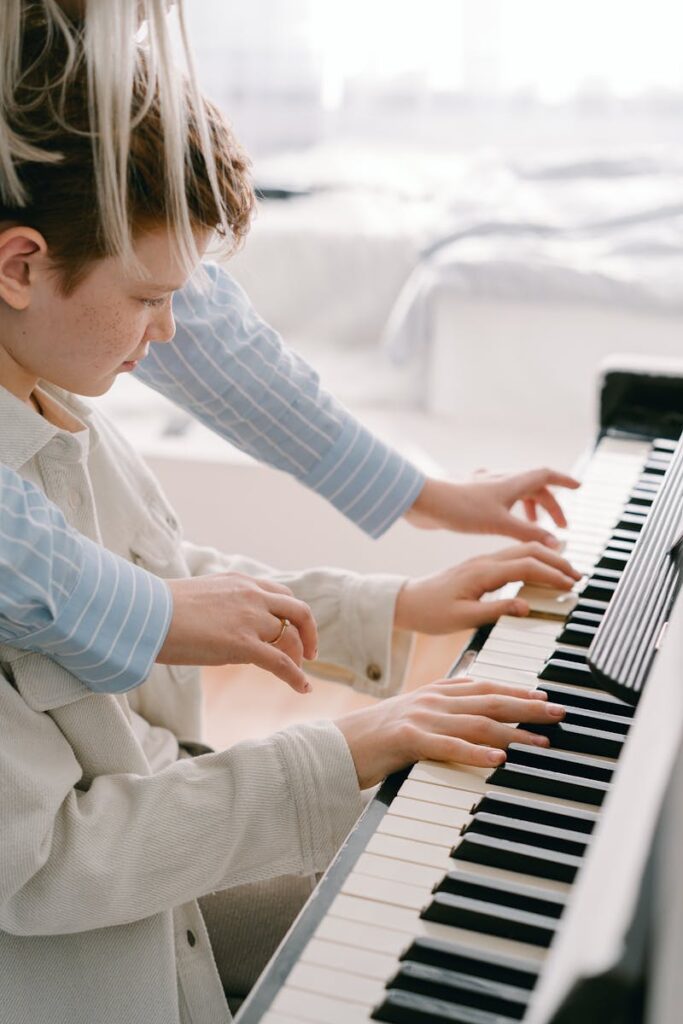 A teenager practices piano under the guidance of a mentor in a cozy indoor setting.